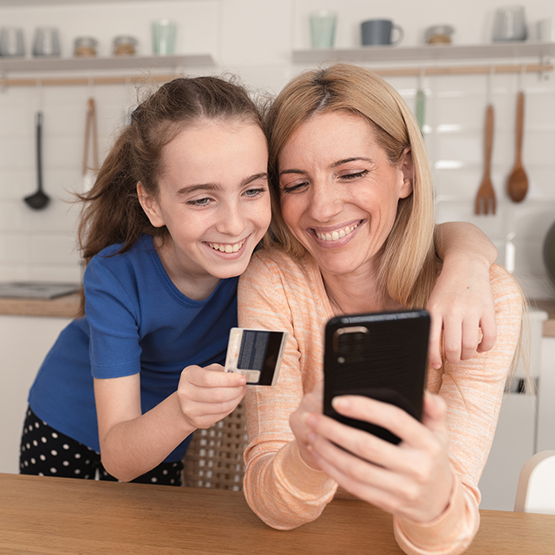 Mom and daughter smile at cell phone  with debit card.